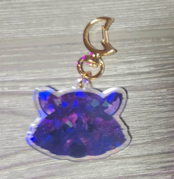 A photo of a purple holographic raccoon keychain with a moon shaped keyring